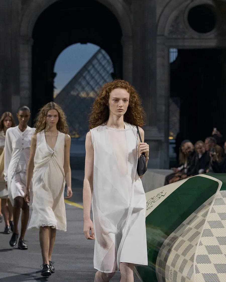 Finale of the Louis Vuitton Spring-Summer 2027 show: models in light white dresses in the Cour Carrée, the Louvre pyramid in the background