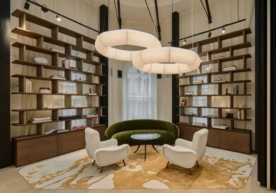 Lounge with wooden bookshelves, white armchairs, a green sofa and ring-shaped lights in the Montblanc boutique in Sydney