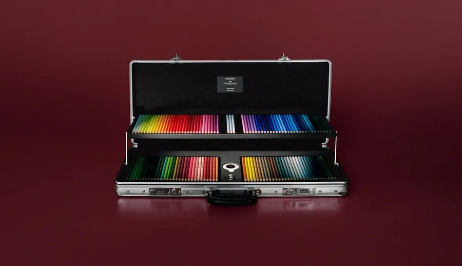 The RIMOWA × Faber-Castell Artist Case, opened on a dark red background, its two trays filled with coloured pencils